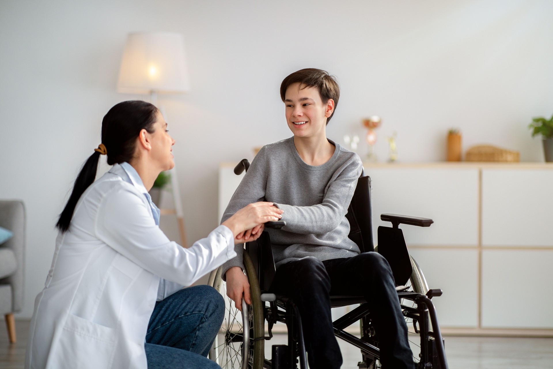 Disabled people healthcare support. Doctor holding hands of handicapped teen boy in wheelchair during medical visit